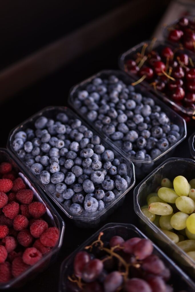 Colorful assortment of fresh berries and grapes in plastic containers, showcasing organic produce in vibrant hues.