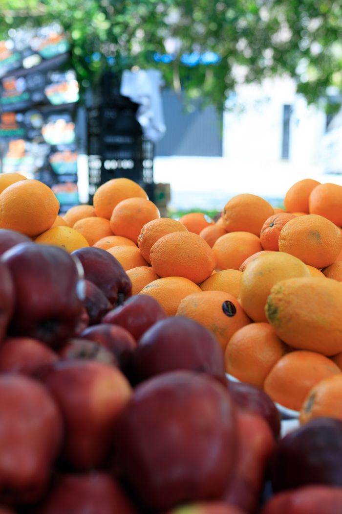 Vibrant oranges and apples on display at an outdoor market stall, highlighting seasonal produce.